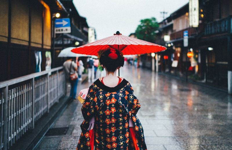 雨の石畳を朱の和傘で歩く着物姿